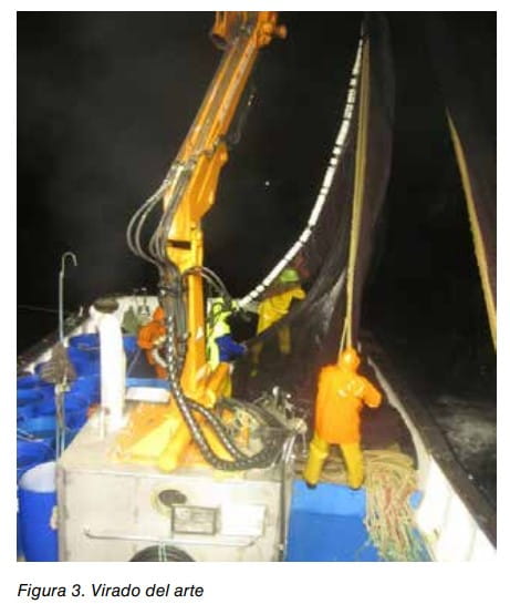 Pescadores en la cubierta de un barco virando el arte de pesca de noche con ayuda de una grúa hidráulica.