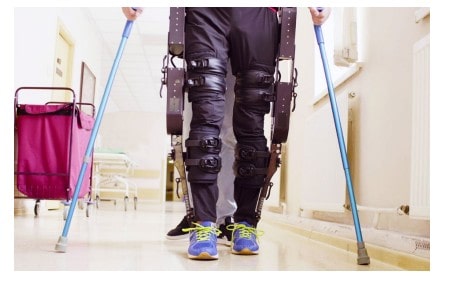 Figura 1: persona con exoesqueleto robótico en las piernas caminando con muletas en un pasillo de rehabilitación.