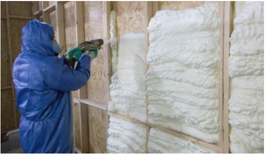 Operario con traje y máscara de protección proyectando espuma aislante sobre una pared con estructura de listones.