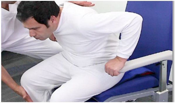 Figura 2: persona vestida de blanco apoyándose en el reposabrazos de una silla durante un ejercicio de movilización