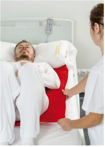 Sanitaria colocando un cojín de posicionamiento bajo el cuerpo de un paciente encamado