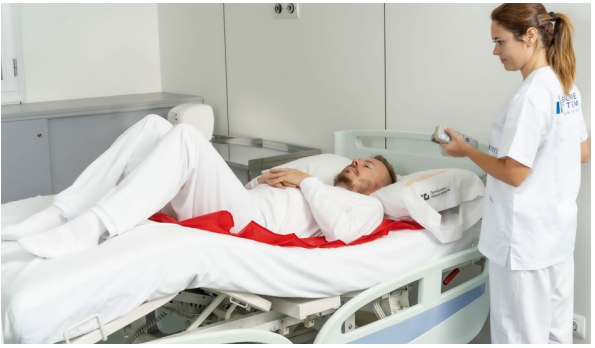 Profesional sanitaria atendiendo a un paciente tumbado en una cama hospitalaria articulada.