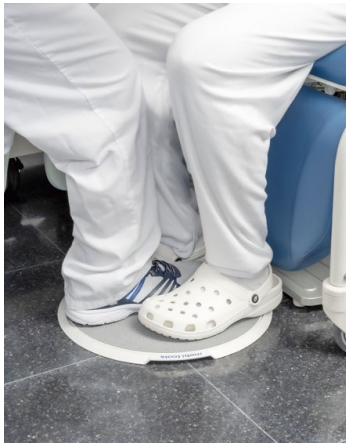 Pies de un trabajador con zuecos sanitarios apoyados sobre una plataforma giratoria de un sillón clínico.