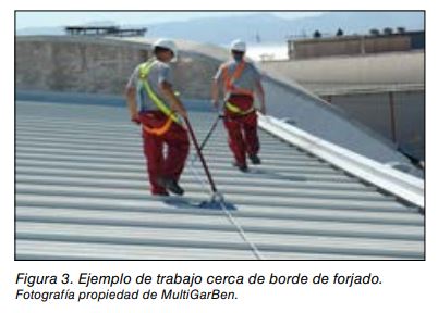 Dos operarios con arnés trabajando sobre una cubierta metálica cerca del borde del forjado