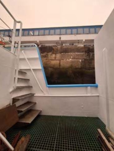 Cubierta de un pesquero de palangre con barandilla perimetral y escalera junto a una abertura lateral.